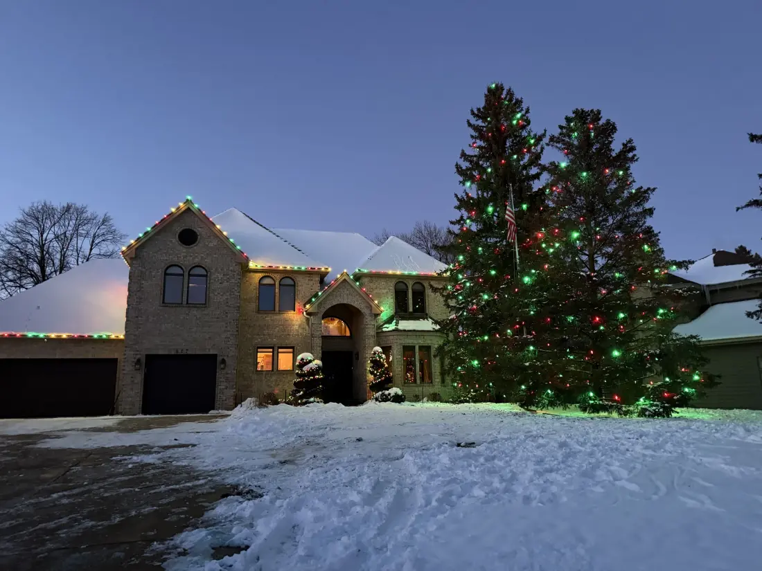 Red and green holiday lighting on a snowy Twin Cities home